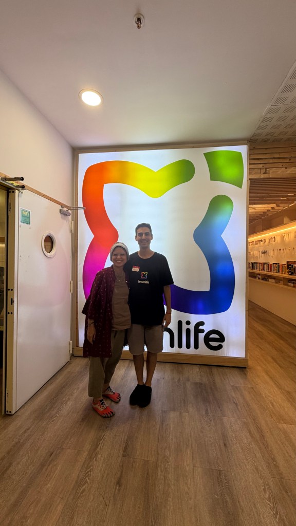 Two people posing together in front of a brightly colored 'Iconlife' sign inside a store.